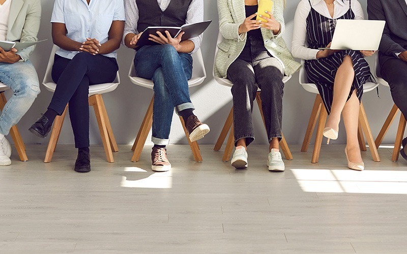 candidates sitting in a row of chairs, holding their resumes and waiting for their interview